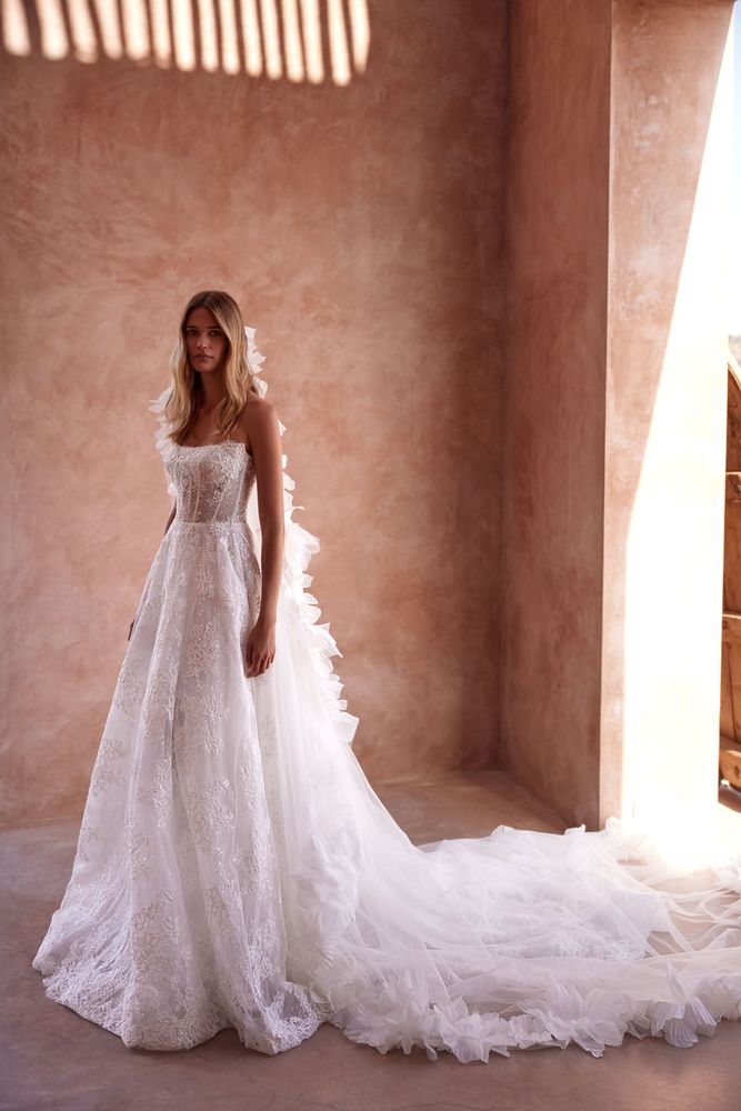 Fairylike A-line wedding gown made from a chantilly lace covered in sequined appliques. Featuring a semi-transparent straight geometric boned corset, lace-up closure on the back, and a semi-transparent fully embellished skirt with a midi train.