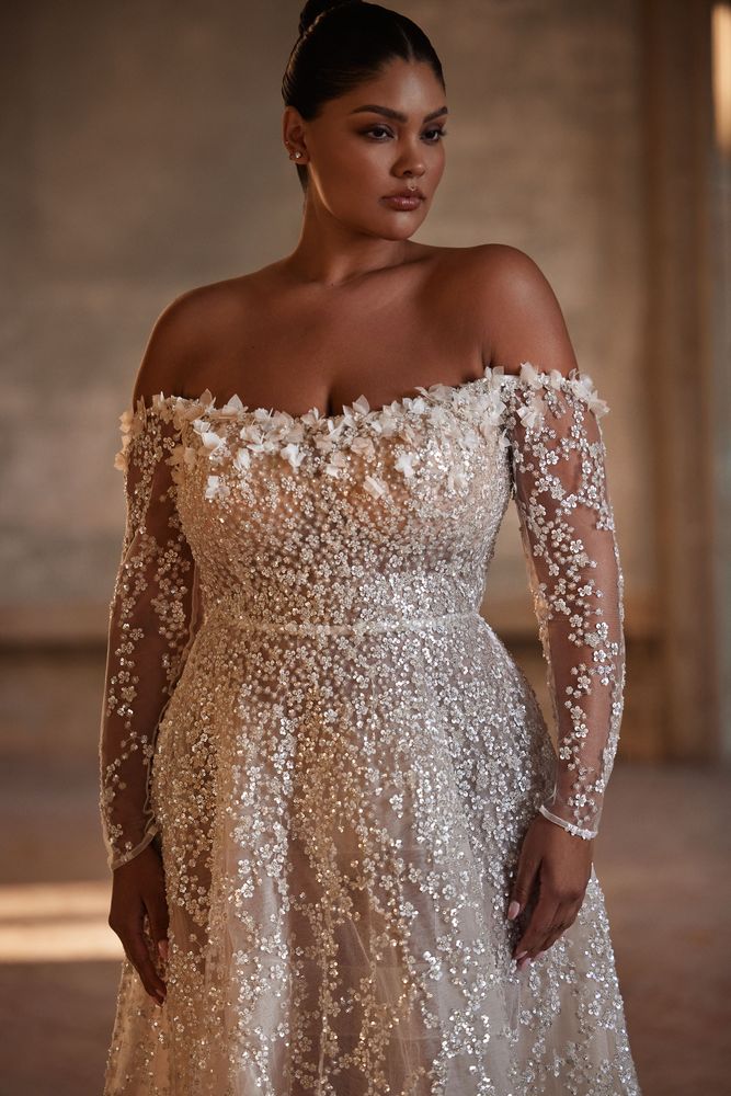 Exquisite semi-transparent wedding gown, fully covered in dramatic sequins and floral embroidery. Featuring off-the-shoulder long sleeves, a straight neckline adorned with flowers, lace-up closure on the back, and a short train.