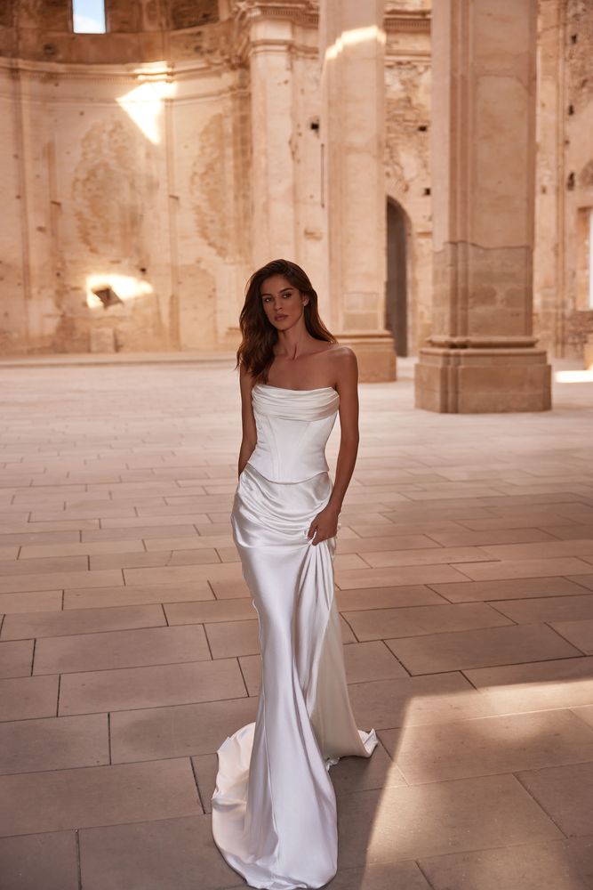 Notable contemporary two-piece wedding look made of lux Italian silk. The corset features a cinched waist and draped neckline inspired by the classic ball gown and a boned corset with a zipline on the back. The corset is doubled, with an additional shaping corset sewn in. The look is finished with a flowy skirt with a midi train reminiscent of ancient Greek statues.